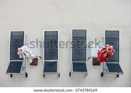 Top Down View of Four Modern Beach Loungers and Folded Umbrellas on Tiled Terrace. High-angle minimalist shot of empty gray sunbeds and closed red and white parasols on a clean stone patio.