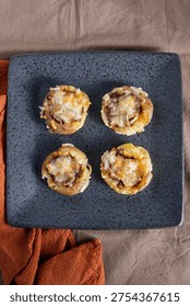 Top down view of four smashed potatoes stuffed with cheese and meat, symmetrically arranged on a dark, textured square plate.