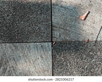 Top down view of four square concrete pavement tiles forming a cross pattern with a single fallen dry leaf lying.
