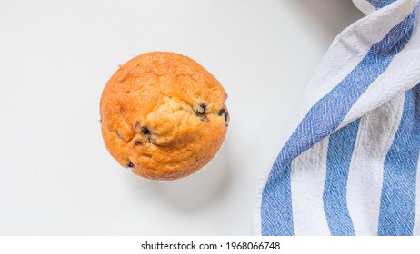 Top Down View Of A Fresh Blueberry Muffin And Tea Towel Against A White Background With Natural Morning Light.