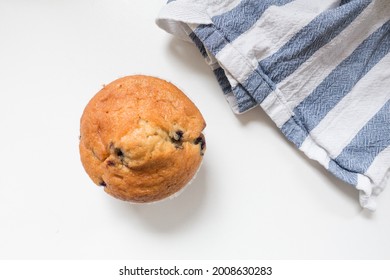 Top Down View Of A Fresh Blueberry Muffin And Tea Towel Against A White Background With Natural Morning Light.