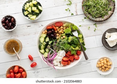 Top down view of a Greek salad bowl with separate bowls of the ingredients.