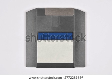 A top down view of a grey magnetic storage disk with a white label and metal protective shutter on a plain white background
