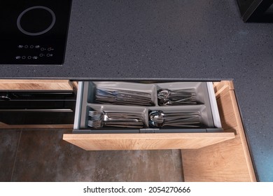 Top down view of a grey stone kitchen counter with open cutlery drawer showing the eating utensils neatly arranged in compartments with copyspace