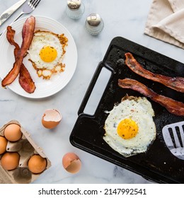 Top down view of a griddle pan cooking bacon and eggs for breakfast. - Powered by Shutterstock