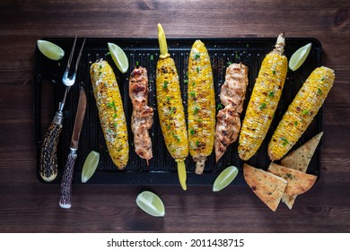 Top Down View Of Grilled Corn On The Cob With Chicken Skewers On A Cast Iron Grill Pan.