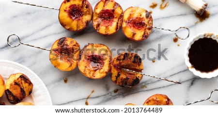 Top down view of grilled peach skewers on a marble slap with sweet barbecue sauce.