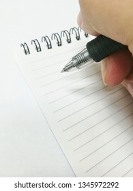 top down view of a hand holding ball point black ink pen on a mini notebook with lines and metal rings to write reminders