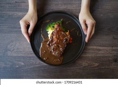 Top down view of the hand holding the barbeque grilled chicken on black ceramic place with wooden table background