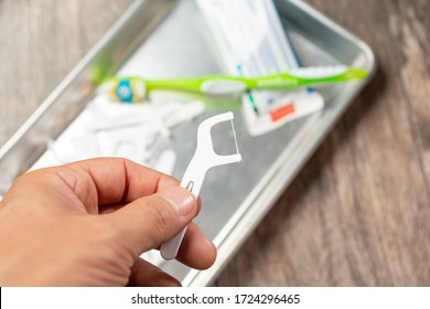 A Top Down View Of A Hand Holding A Flosser, Over A Tray With More Flossers, A Toothbrush, And A Tube Of Toothpaste.