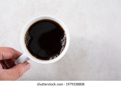 A Top Down View Of A Hand Holding A Cup Of Black Coffee.