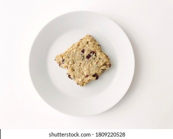 Top Down View Of Healthy Granola Bar Square With Fruits On White Plate Against A White Background.