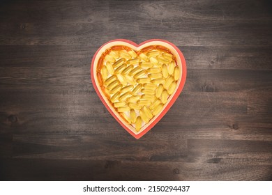 Top Down View Of A Heart Shaped Box Filled With Omega 3 Fish Oil Pills On A Wooden Table Surface