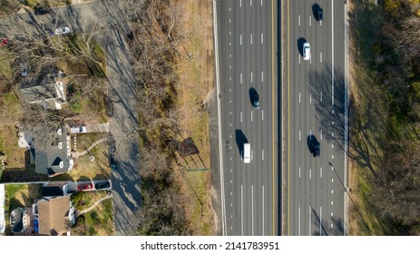 A Top Down View, High Over A Suburban Neighborhood With A Wide Road, With A Few Cars Traveling On It. Taking With A Drone On A Sunny Day.