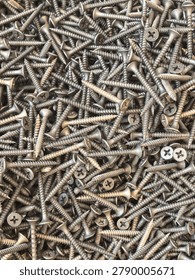Top down view of hundreds of small Phillips head screws scattered randomly creating a full frame metallic texture and industrial background.