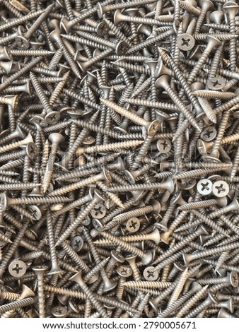 Top down view of hundreds of small Phillips head screws scattered randomly creating a full frame metallic texture and industrial background.