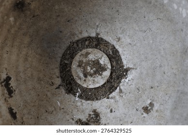 Top down view of the inside of an empty, weathered ceramic plant pot. Visible dirt, soil residue, and a drainage hole at the bottom with a gritty texture.