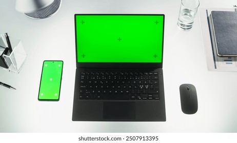 Top Down View of a Laptop Computer with Mock Up Green Screen Standing on an Office Desk Next to a Smartphone with a Template Chromakey Display with Motion Tracker Placeholders. Workplace Concept.