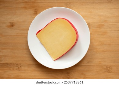 A top down view of a large slice of gouda cheese, on a plate.