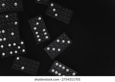 Top down view of left aligned scattered domino pieces with various dotted numbers across a black surface with copy space on the right