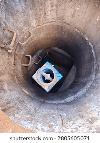 Top down view looking into a deep concrete utility manhole shaft with rusty metal steps and a blue fire hydrant at the bottom.