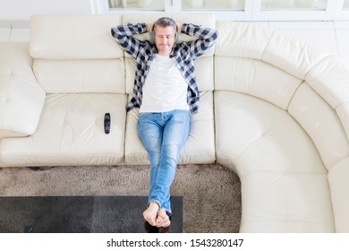 Top Down View Of Mature Man Relaxing On Sofa With Headphones In The Living Room. Shot At Home