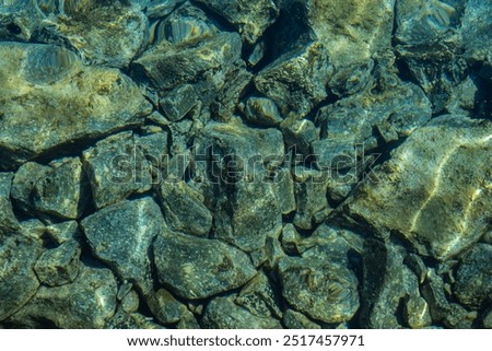 Top down view of mesmerizing view of stones submerged in the crystal-clear waters of the sea. The rocks, of various sizes and shapes, appear to have a greenish and grayish hue. Agios Nikolaos, Crete 