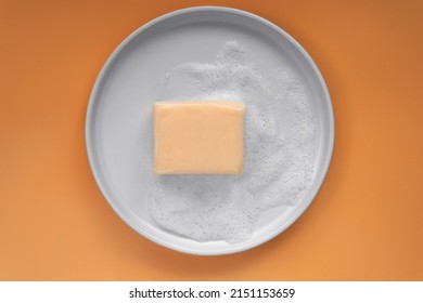 Top Down View Mockup Peach Pastel Orange Color Vitamin C Soap Bar Square Shape With Foam Bubbles Water On White Plate And Solid Plain Orange As Background