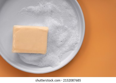 Top Down View Mockup Peach Pastel Orange Color Vitamin C Soap Bar Square Shape With Foam Bubbles Water On White Plate And Solid Plain Orange As Background