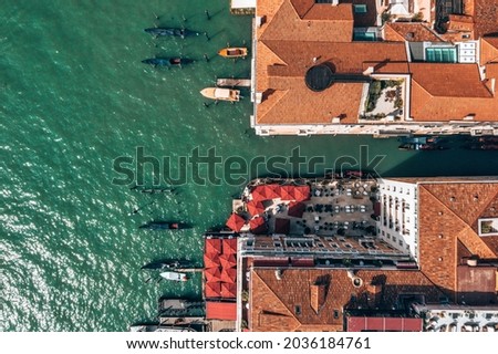 Top down view of moored empty venetian gondolas and old stone bridge on a narrow water canal in Venice, Italy.