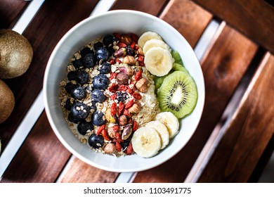 Top Down View Of A Muesli Bowl With Yogurt, Fruits And Nuts On A Wooden Table