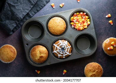 Top Down View Of A Muffin Tin With Baked Cupcakes And Halloween Decorations. 