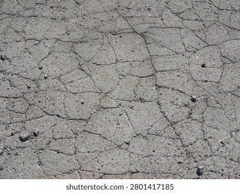 Top down view of old cracked asphalt texture background with a network of fissures and small stones.