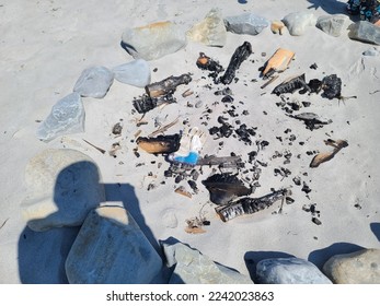 A top down view of an old firepit left on a sandy beach with a shadow in the corner. An old work glove has also been left inside of it.