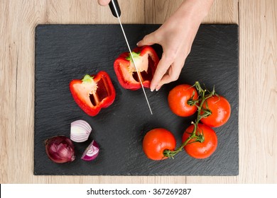 Top down view on black slate cutting board with hands cutting and slicing vegetables. - Powered by Shutterstock