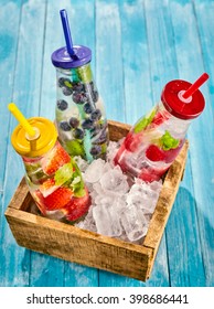 Top down view on bottles full of ice water and strawberries, blueberries and raspberries in a little box on top of wooden table