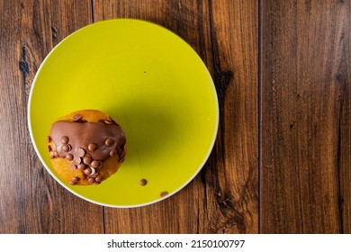 Top Down View On A Chocolate Chip Muffin On A Yellow Plate And Wooden Table. Copy Space.