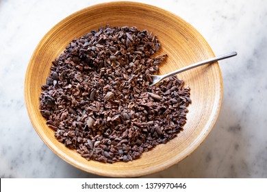 Top Down View On Cocoa Nibs In A Wooden Bowl, On A White Marble Counter, In A Chocolate Ingredient Background