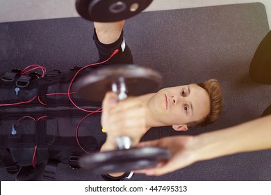 Top Down View On Male Person In Biometric Fitness Vest Using Dumbbells With Hands Of Spotter Nearby