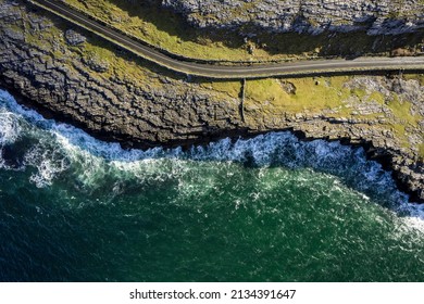 Top down view on a small road by a rough stone coastline. Rock formation and ocean water surface. Burren, Ireland