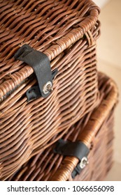 Top down view on stack of antique wicker picnic baskets, made of woven willow branches, and selective focus on the metal latch and black leather strap locking the lid