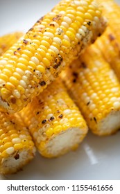 Top Down View On A Stack Of Barbecued Corn On The Cob, With Charred Kernels, On A White Dinner Plate