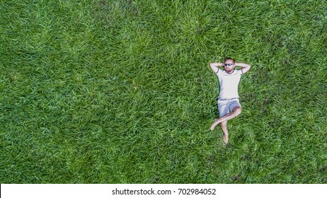 Top Down View On A Young Man Wearing Sun Glasses And Lying On A Vivid Juicy Green Grass Relaxing In A Hot Summer Day