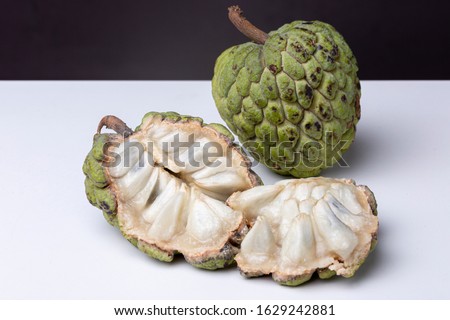 Top down view of opened up and intact Sugar-apple or 'Fruta de Conde' [Earl Fruit] as it is known in Brazil on a white surface with dark background showing inside with fleshy 'teeth' and outside peel