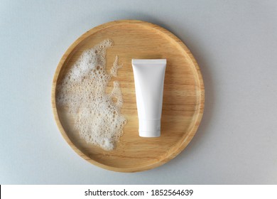 Top Down View Of Organic Gentle Facial Skincare Product Cleanser White Tube With Soap Bubbles And Blank Label On Bamboo Wooden Plate Grey Blue Cardboard Box Paper Background.