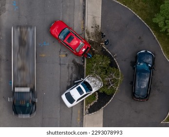 A top down view of a parked black car, next to a recent automobile accident involving two other cars. Taken on a cloudy day in a residential neighborhood as a tow truck arrives on the scene.