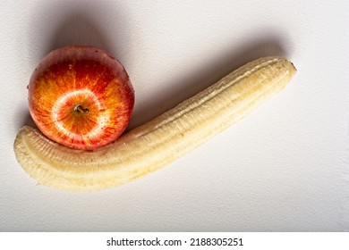 Top Down View Of Peeled Banana In Shape Of Checkmark Complemented With Bright Red Gala Apple On White Cutting Board. Copy Space