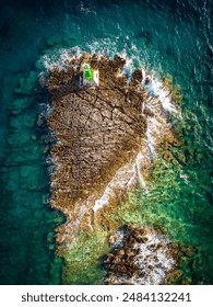Top down view of Punta Planka green lighthouse on the sharp rocks submerged in turquoise adriatic sea near town of Rogoznica, Croatia