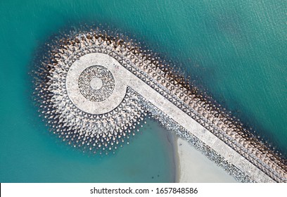 Top down view of a q-shaped jetty, reinforced with tetrapods (concrete wave breaker blocks), extruding into the turquoise sea water to protect the coast from erosion, on Yuguang Island, Tainan, Taiwan