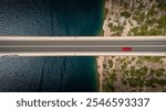 Top down view of a red car alone driving on a bridge over the sea. Background images for travel, holidays, the beauty of traveling by car to discover a country. Maslenica bridge, Croatia.